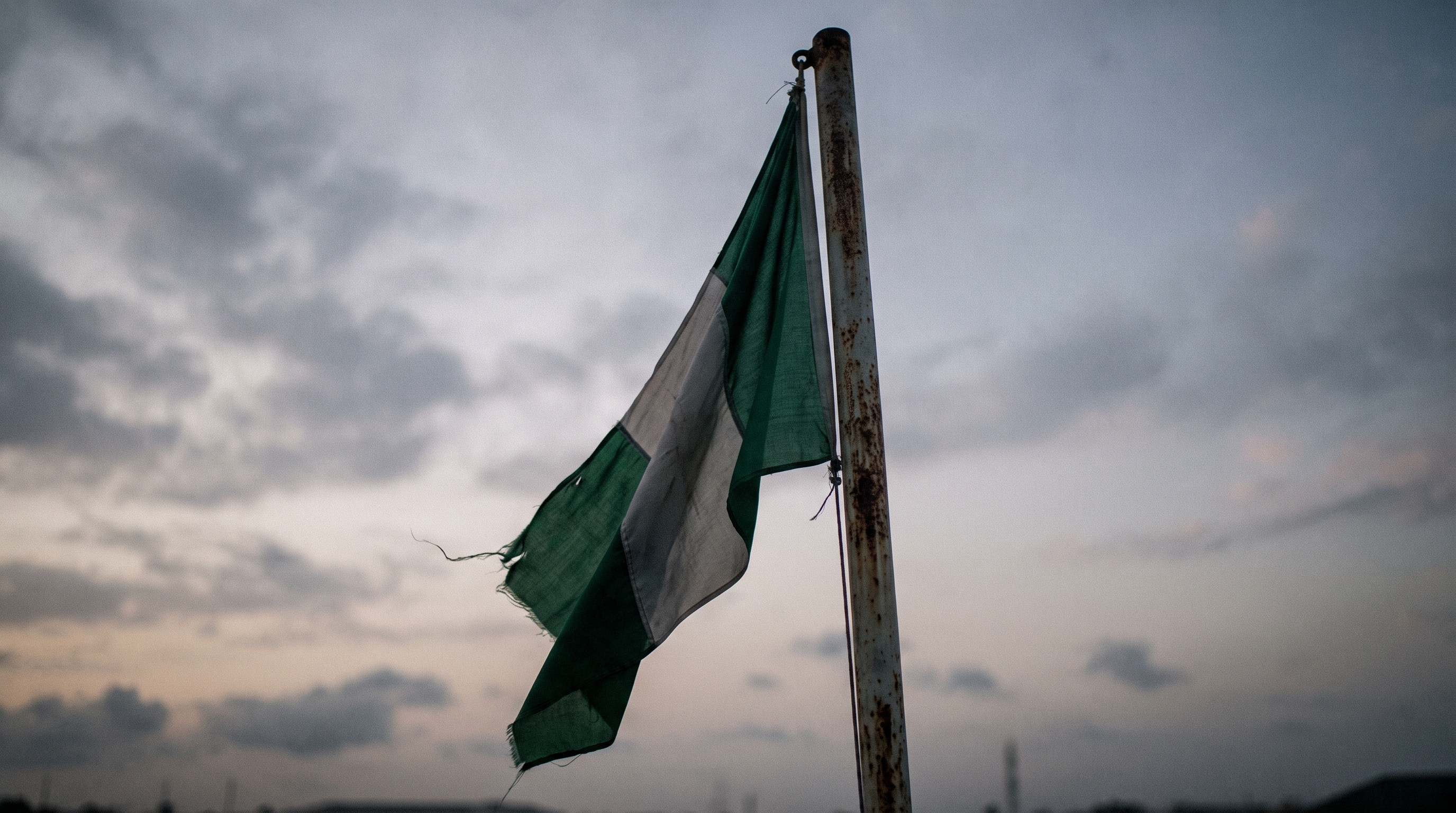 A Nigerian flag hanging still against a pale evening sky
